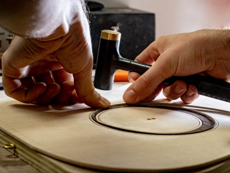 Mains du luthier FP Guitars incrustant un filet en bois dans une rosace à l’aide d’un marteau, illustrant la précision du travail artisanal et le soin apporté aux finitions esthétiques.