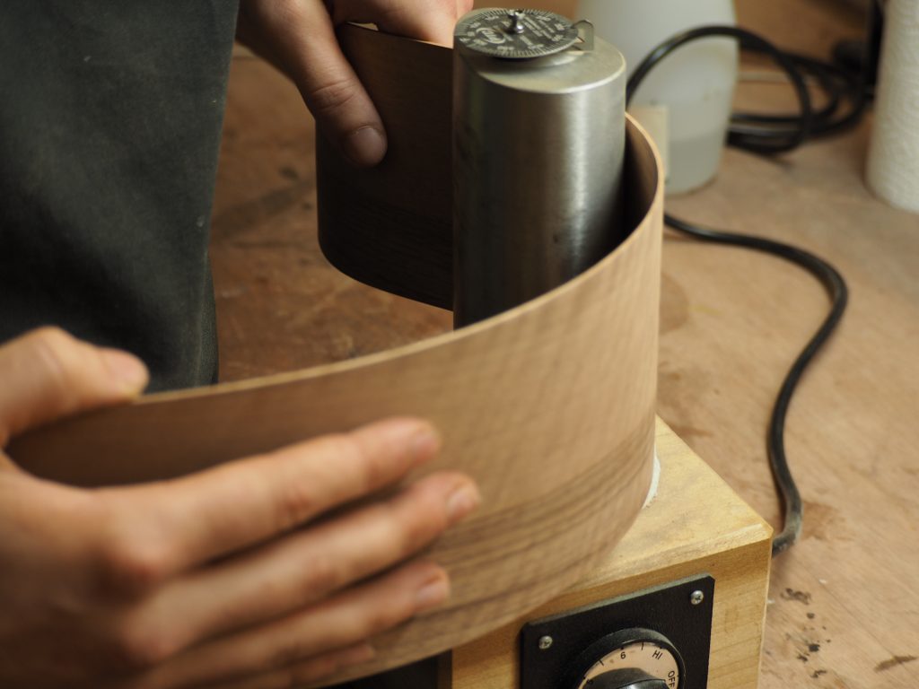 Mains du luthier FP Guitars en train de cintrer une éclisse en noyer sur un fer à cintrer, illustrant le travail artisanal précis réalisé à la main dans l’atelier entre Annecy et Genève.