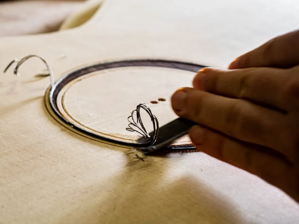 Mains du luthier FP Guitars ajustant une rosace à la main au ciseau, un copeau fin révélant la précision du travail artisanal et le soin apporté aux détails.