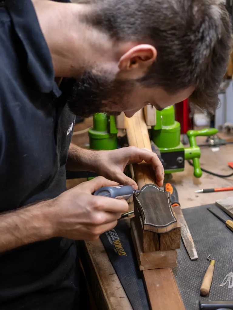 Incrustation manuelle d’un filet en nacre dans une tête de guitare en ébène et acajou, réalisée à la main dans l’atelier FP Guitars.