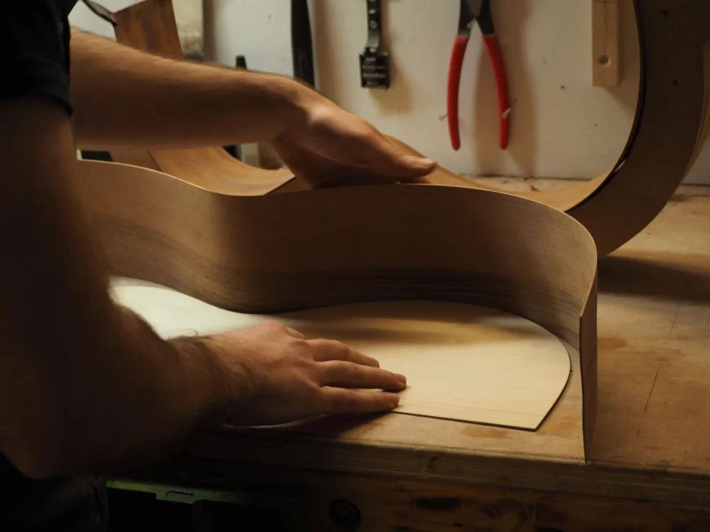 Luthier FP Guitars en train de cintrer une éclisse en noyer sur fer chaud, geste précis et contrôlé, avec mise en avant du travail artisanal haut de gamme.