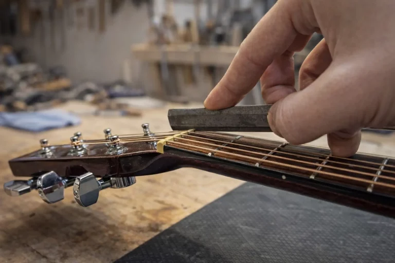 Réglage précis du sillet de tête sur une guitare acoustique à l’atelier FP Guitars, contrôle de la hauteur des cordes et du relief du manche par un luthier professionnel