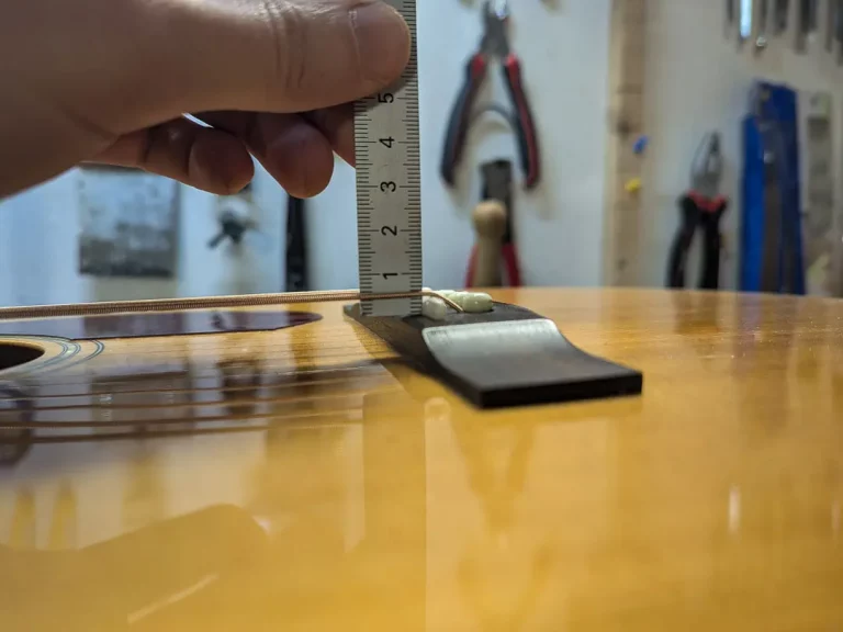Mesure de la hauteur des cordes au chevalet sur une guitare acoustique à l’aide d’une règle, étape clé du réglage de l’action et du confort de jeu