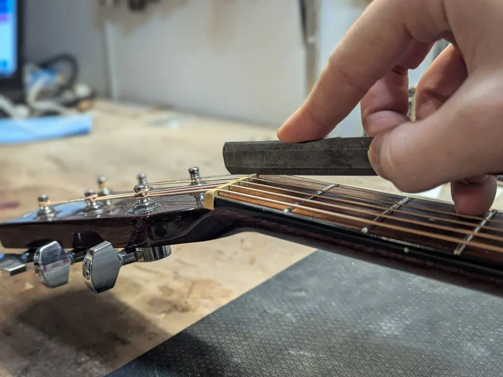 Réglage précis du sillet de tête sur une guitare acoustique à l’atelier FP Guitars, contrôle de la hauteur des cordes et du relief du manche par un luthier professionnel
