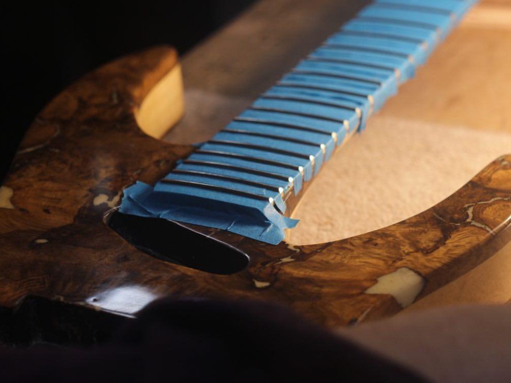 Guitare électrique artisanale FP Guitars en phase de préparation, la touche protégée par un ruban de masquage avant le polissage des frettes, symbole du soin apporté aux réglages et à la finition de chaque instrument.
